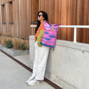 Frau mit langen, dunklen Haaren und buntem Pulli trägt upcycelten Rucksack in rosa mit blauen Fischen