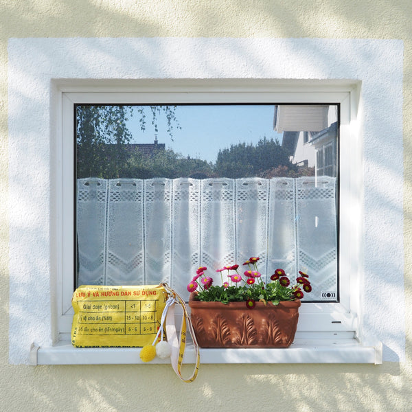 Gelbe Umhängetasche mit Bommeln steht am Fensterbrett neben einem Blumentopf