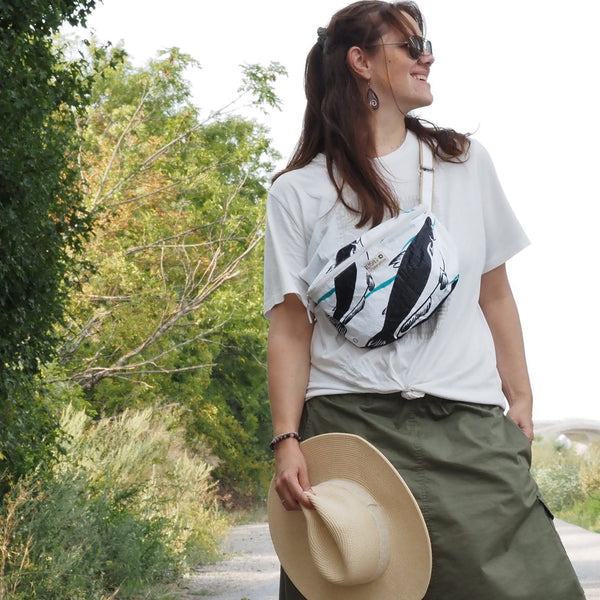 lachende Frau trägt die weiße Bum Bab crossbody und hält einen Hut in der Hand