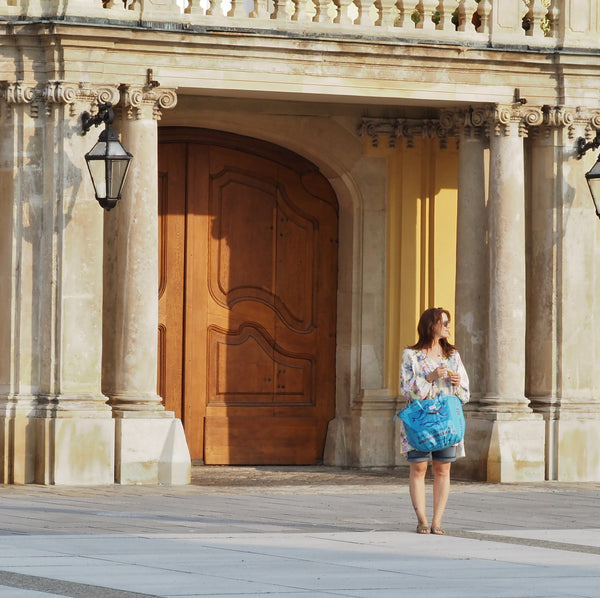 Frau steht in der Abendsonne und hält eine blaue Badetasche in der Hand