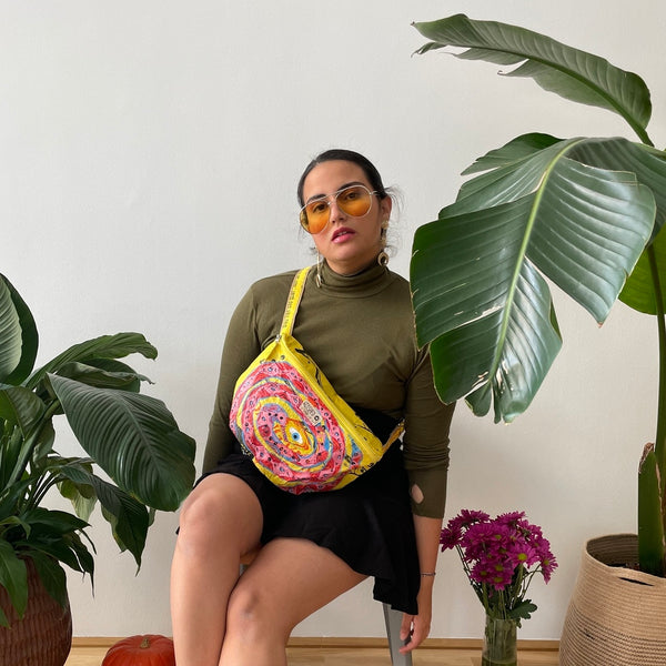 Frau sitzt neben einer großen Zimmerpflanze und trägt eine gelbe Bauchtasche