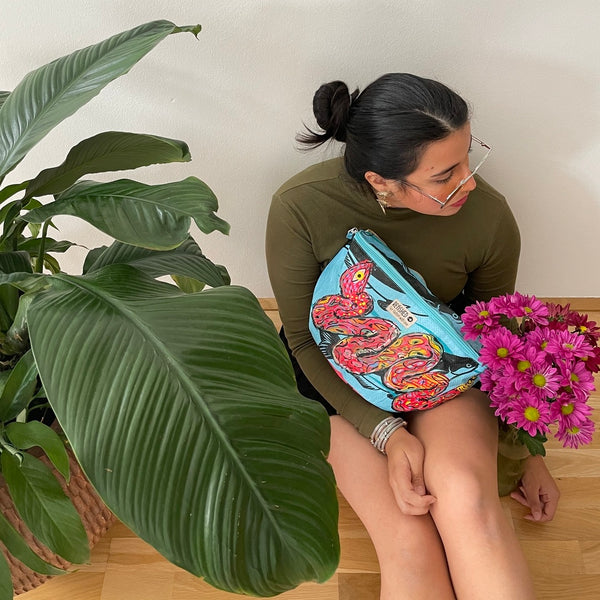 Frau sitzt neben einer Zimmerplanze und trägt eine blaue Bauchtasche