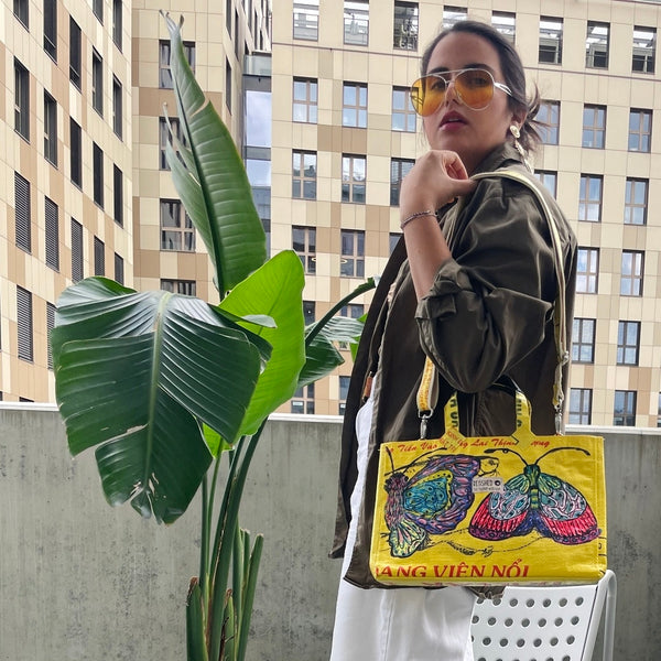 Frau steht in der City am Balkon und trägt die gelbe Isolde Bag lässig um den  Arm