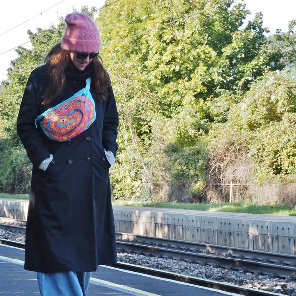 Frau geht mit blauer Bauchtasche an einem Bahnsteig entlang