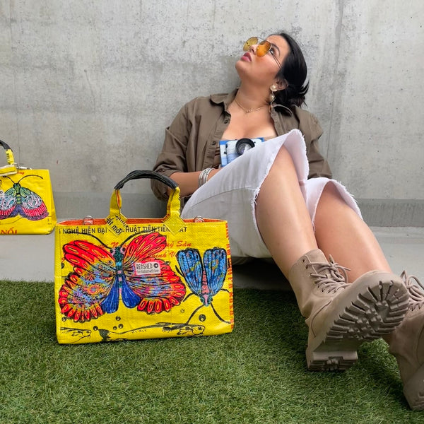 Frau sitzt mit gelber Tasche mit buntem Schmetterlingsmotiv am Boden