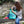 Load image into Gallery viewer, Frau öffnet grünen Rucksack mit Fischmotiv auf einer Steinbank sitzend
