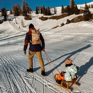 Vater mit Mountain Rucksack zieht die Tochter auf einer Rodel durch den Schnee