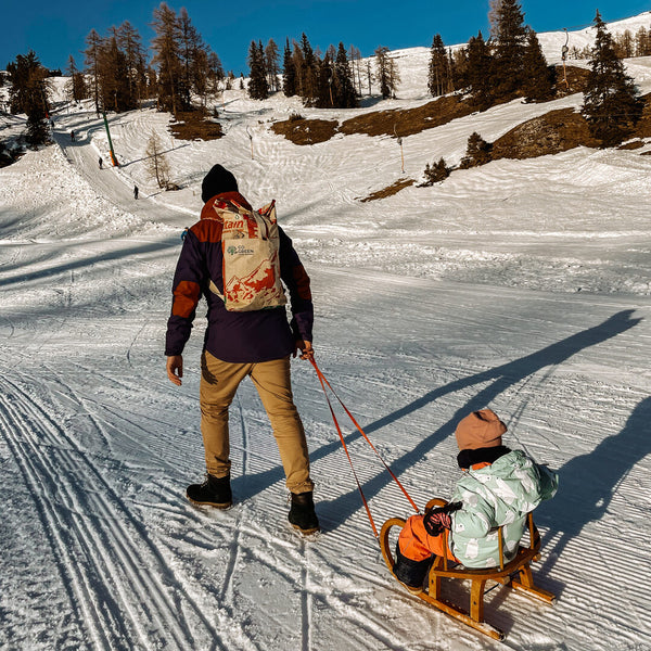 Vater mit Mountain Rucksack zieht die Tochter auf einer Rodel durch den Schnee