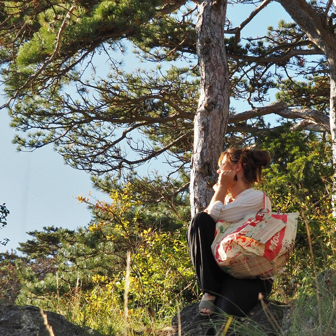 Frau sitzt mit Shopper mit Bag-in-Bag bei Sonnenuntergang im Wald