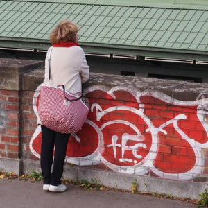 Frau steht mit rot-weißer TWEED Soulmate an einer Mauer mit rotem Graffiti und sieht in die Ferne