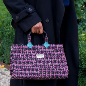 lila-schwarze Isolde Tasche wird an den kurzen Henkeln in der Hand gehalten