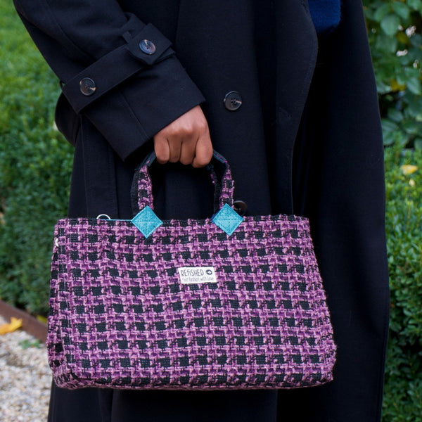 lila-schwarze Isolde Tasche wird an den kurzen Henkeln in der Hand gehalten