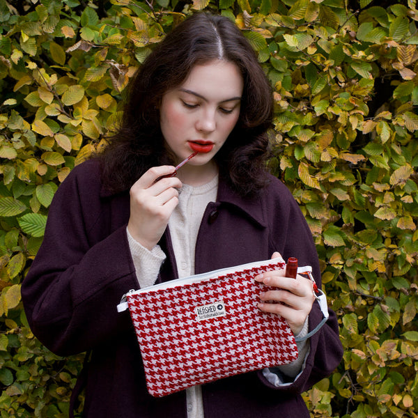junge Frau schminkt sich und hält dabei rot-weißes Täschchen in der Hand