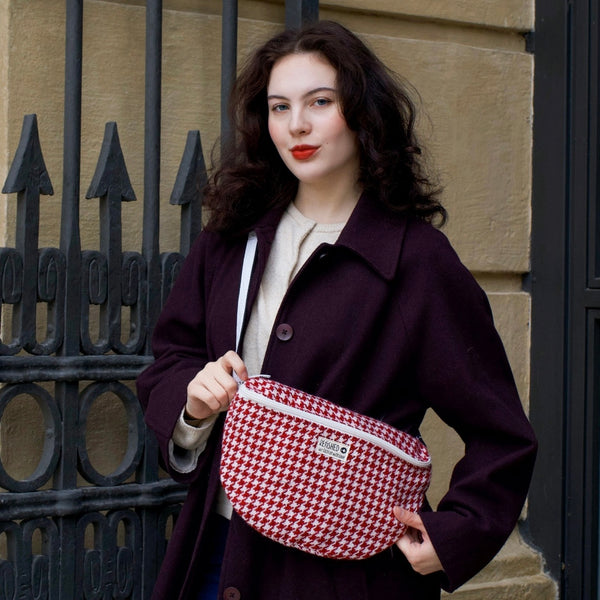 junge Frau mit weinrotem Mantel trägt eine rot-weiße Tasche aus TWEED