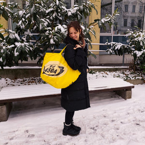 Frau in schwarzem Mantel steht mit gelber Soulmate Tasche vor einer verschneiten Bank