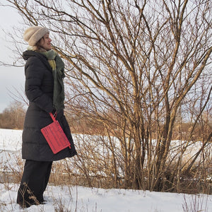 Frau steht mit kleiner, roter Bag-in-Bag in winterlicher Landschaft