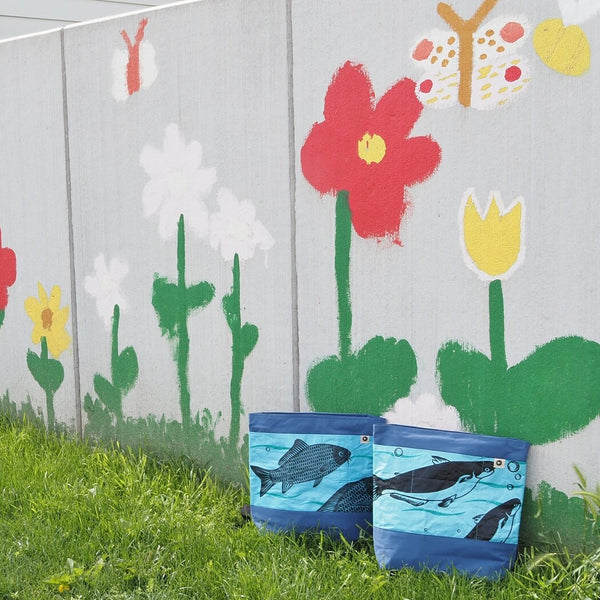 Zwei blaue, fair produzierte Rucksäcke stehen vor einer von Kindern bemalten Wand