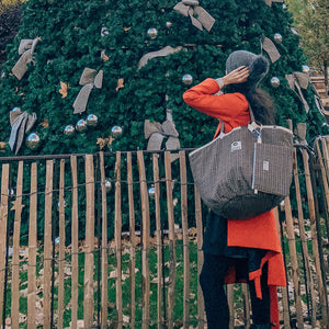 Frau in rotem Mantel und Haube mit beigem Shopper aus TWEED sieht zu einem großen Christbaum hinauf