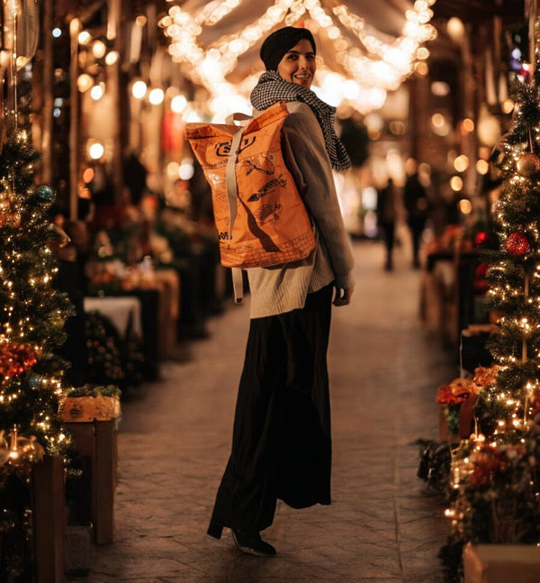 Frau mit orangem Rucksack steht in weihnachtlich geschmückter Gasse / background AI generated