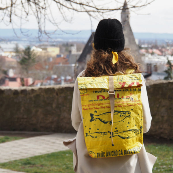 Frau mit Haube trägt gelben Rucksack am Rücken und sieht in die Ferne