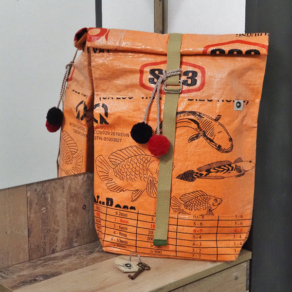 Rucksack orange mit Fischmotiv und Bommeln vor einem Spiegel