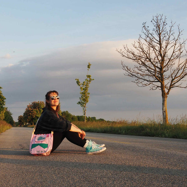 Frau sitzt in der Abendsonne auf dem Boden und hat eine rosa Tasche quer um den Körper