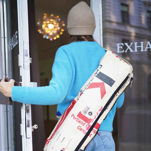 Frau mit blauen Pulli und Haube trägt beige Yogatasche crossbody und betritt das Studio